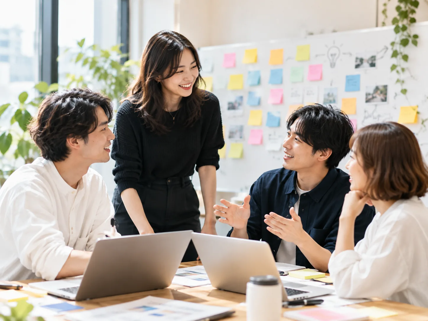 付箋の貼られた壁の前で話し合う4人(イメージ)